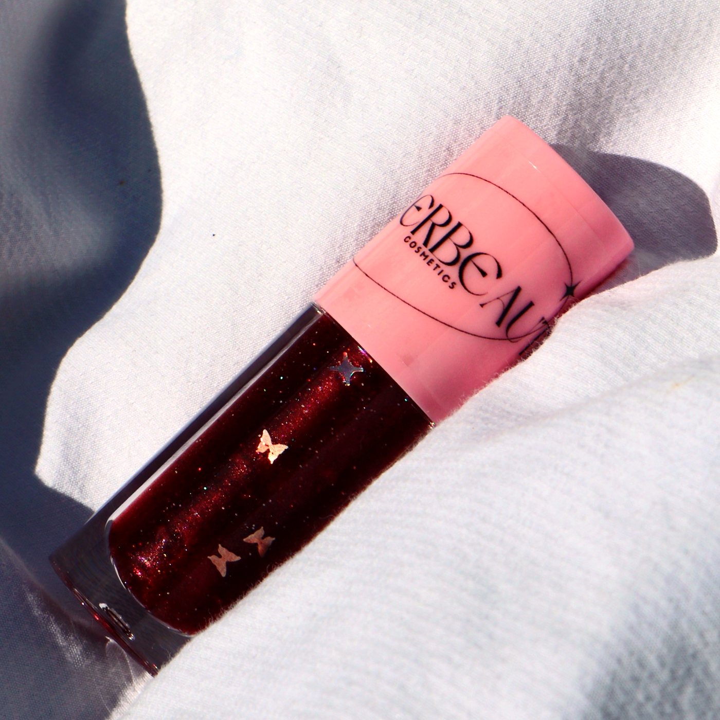 Desire, a deep red glitter gloss with butterfly flecks in a pink-capped MEERBEAUT wand tube on white linen