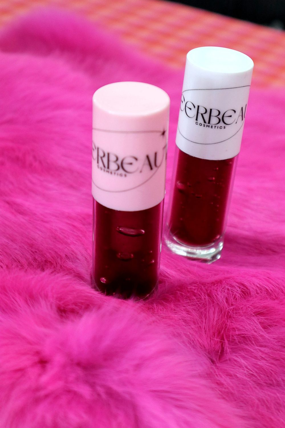 Two MEERBEAUT glosses with pink and white caps standing on pink fur