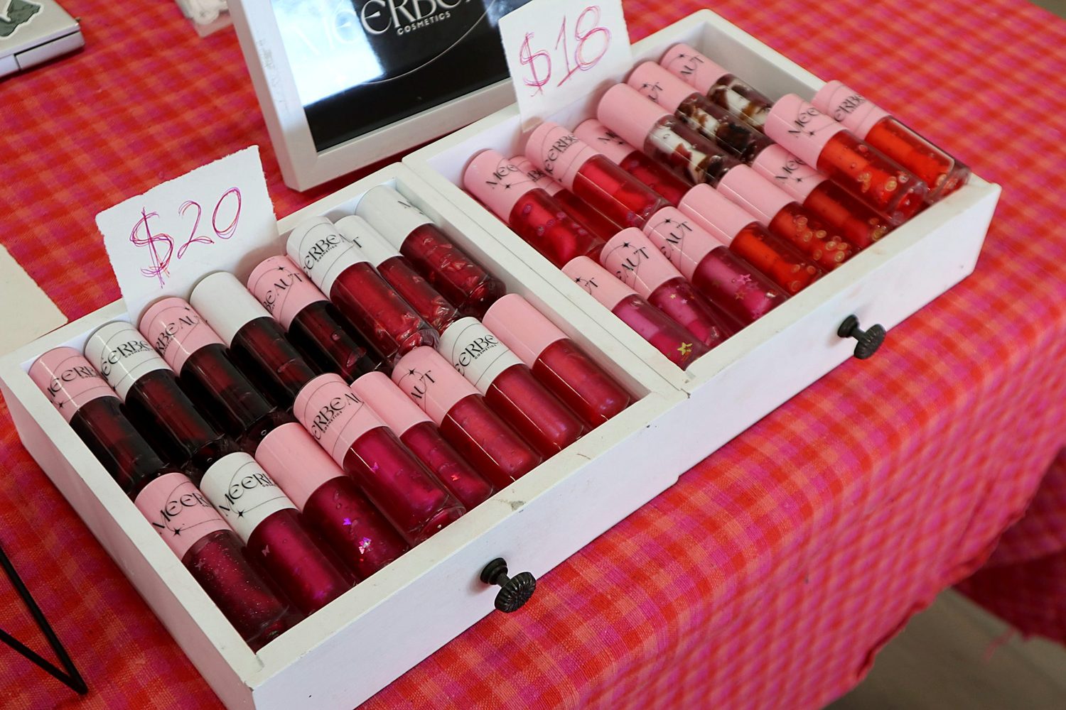 Trays of MEERBEAUT glosses in red, berry and pink shades at our market table